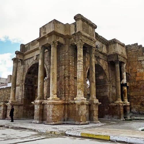The Roman Arch of Caracalla in Tébessa, a weathered stone gateway with columns set against the city walls.