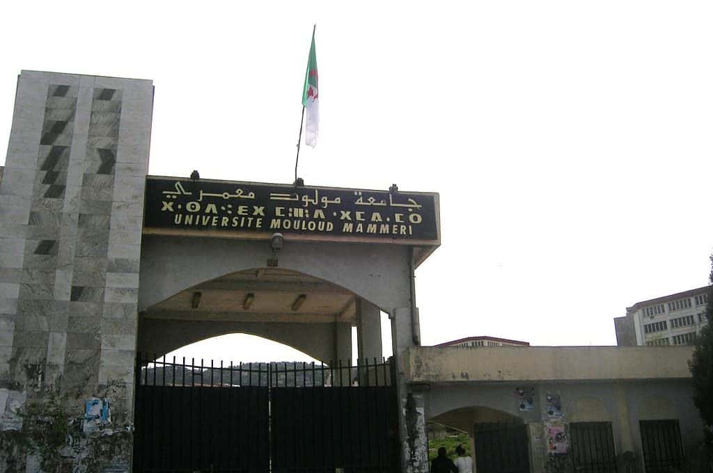 Entrance gate of Université Mouloud Mammeri in Tizi Ouzou, with trilingual signage and an Algerian flag.
