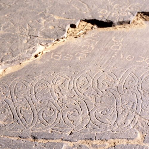 Tifinagh (Amazigh) letters carved into a Saharan rock surface.