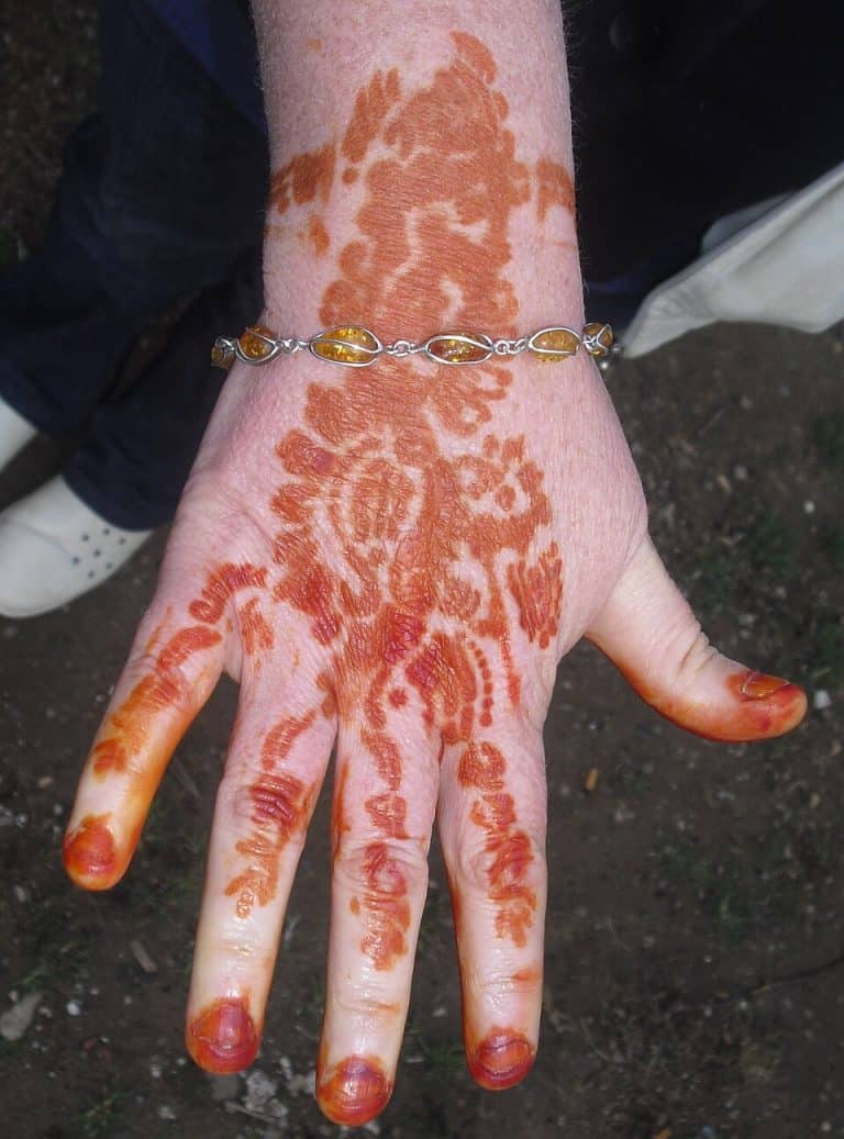 A hand with reddish-brown henna designs on the fingers, palm, and wrist.
