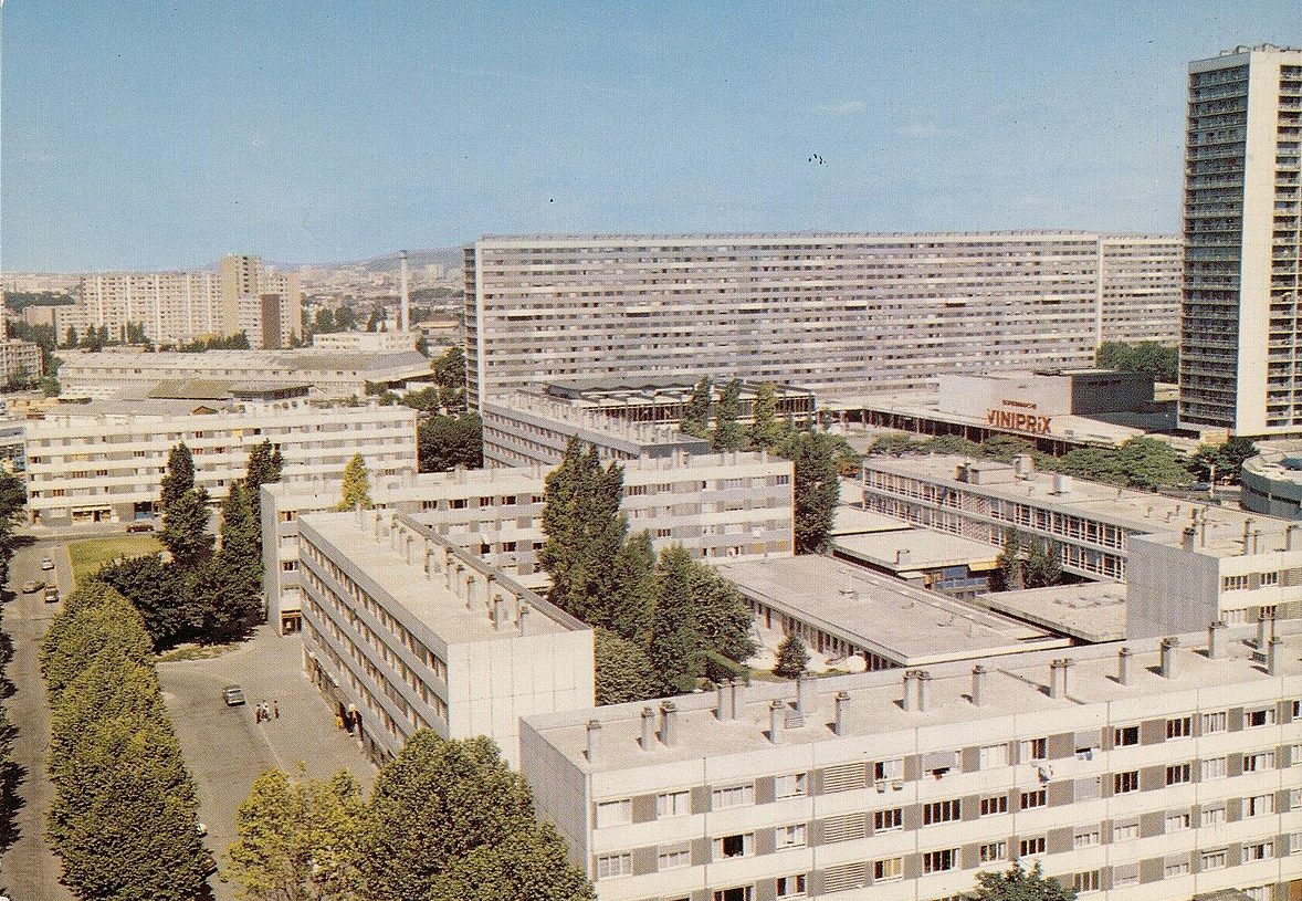 Black-and-white aerial view of large apartment blocks in La Courneuve’s Cité des 4000 housing estate, with surrounding roads and open spaces.