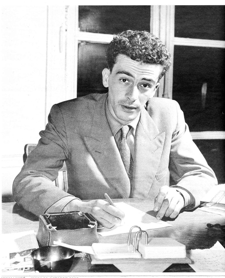Black-and-white photograph of Algerian writer Kateb Yacine seated at a desk and signing a copy of Nedjma in 1956.