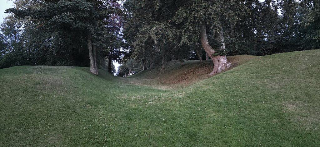 Grassy defensive ditch and earthworks of the Antonine Wall running between tree-lined banks near Falkirk, Scotland.